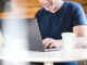 Happy man using laptop with take away coffee cup on table.