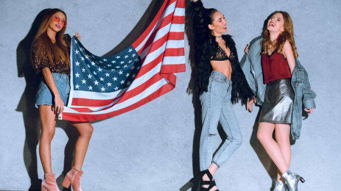 multicultural young women with american flag against concrete wall