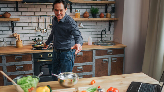 Cheerful man stand at stove and cook food in kitchen.