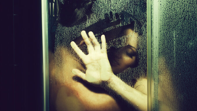 Young couple of naked women and men taking shower with water drops embracing in passion with wet bodies with hand on glass