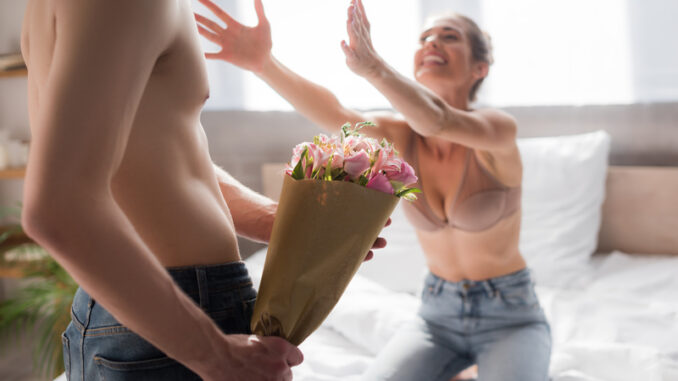 Shirtless men holding flowers near excited women with outstretched hands on blurred background