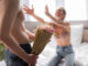 Shirtless men holding flowers near excited women with outstretched hands on blurred background