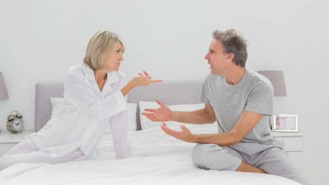 Couple arguing in bedroom sitting on bed