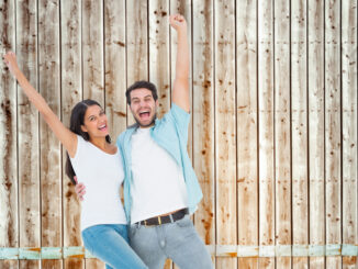 Happy casual couple cheering together against faded pine wooden planks