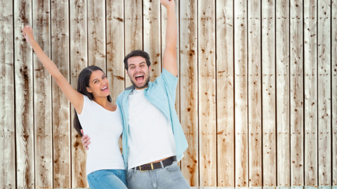 Happy casual couple cheering together against faded pine wooden planks