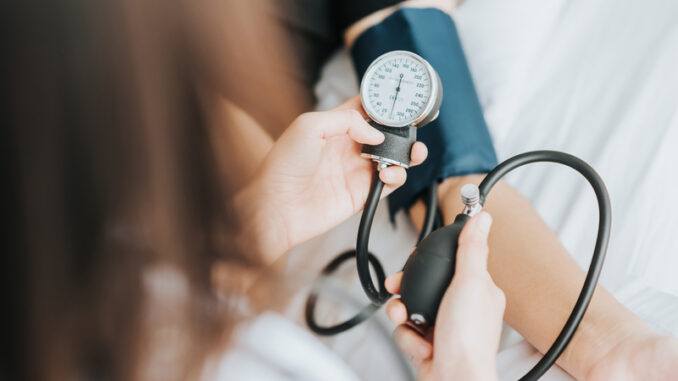 Back view of doctor checking blood pressure of a patient with sphygmomanometer in bed