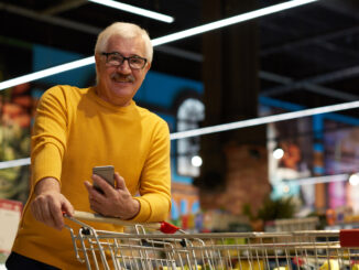 Portrait of modern senior man grocery shopping in supermarket pulling shopping cart and smiling