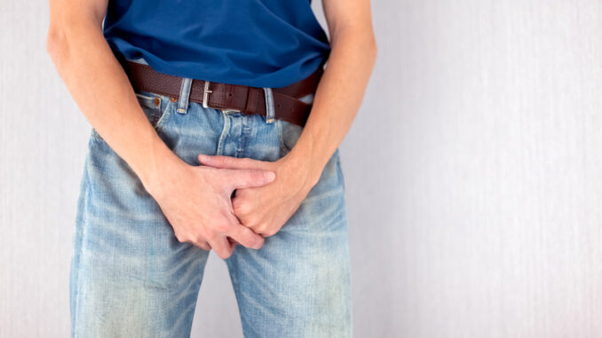 Man in jeans covers his crotch with hands