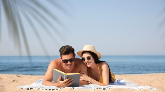 Happy couple reading book together on sunny beach