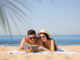 Happy couple reading book together on sunny beach