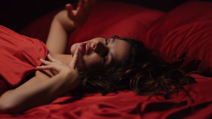 Seductive woman lying on red satin cloth in bed.