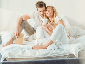young happy couple drinking coffee in bed at morning