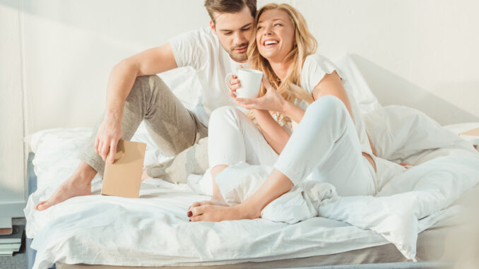 young happy couple drinking coffee in bed at morning