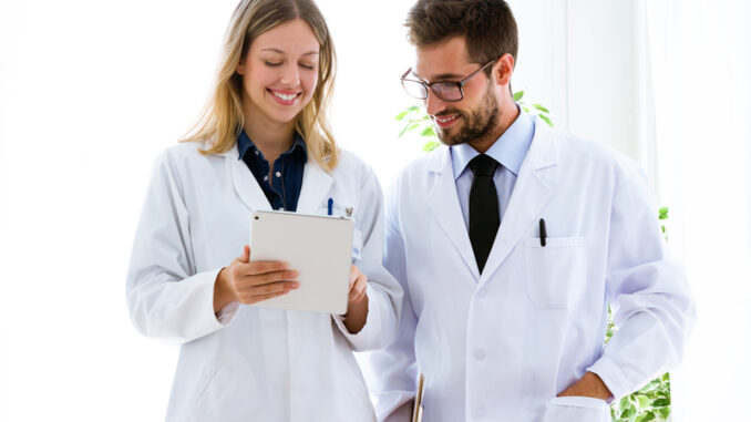Shot of smiling young doctors looking medical reports in digital tablet in medical office