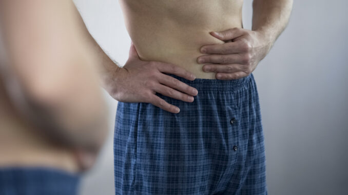 Middle-aged man looking in mirror at his tummy