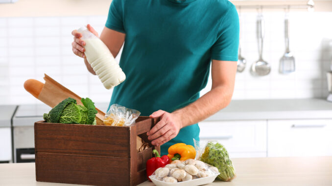 Man with wooden crate full of products at table in kitchen.