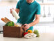 Man with wooden crate full of products at table in kitchen.