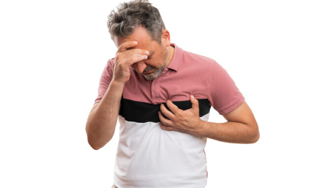 Adult man in colourful fashionable modern summer attire touching chest and head making migraine heart-attack gesture as healthcare