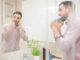 Man standing in bathroom, brushing teeth and having phone call.