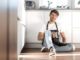 Young man with a glass of water sitting on the floor in the home kitchen.