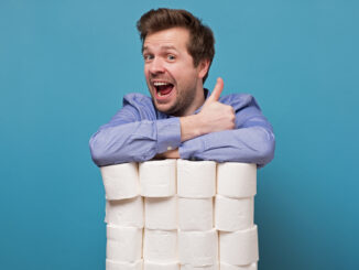 Excited happy caucasian man holding a pile of toilet paper showing thumb up isolated on blue background.