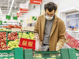 A young man in a medical mask is choosing fruits in a large supermarket.