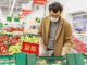 A young man in a medical mask is choosing fruits in a large supermarket.