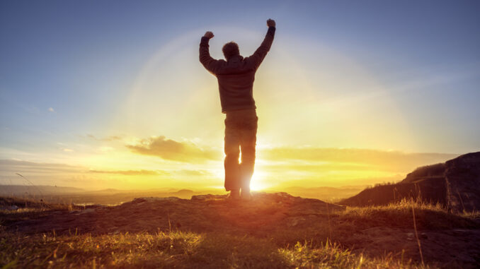 Happy man celebrating winning success or worship and praise against sunset