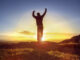 Happy man celebrating winning success or worship and praise against sunset