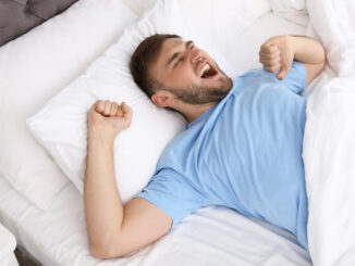 Young happy man waking up after sleeping in bed at home.