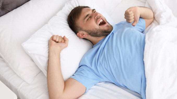 Young happy man waking up after sleeping in bed at home.