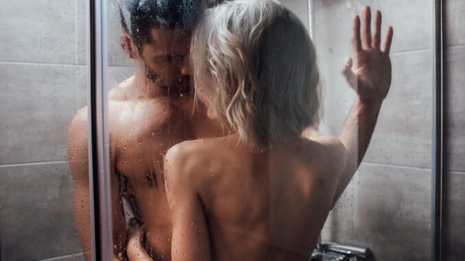 nude heterosexual couple looking at each other, embracing and taking shower together