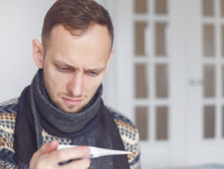 Sick man lying on sofa checking his temperature at home in the living room