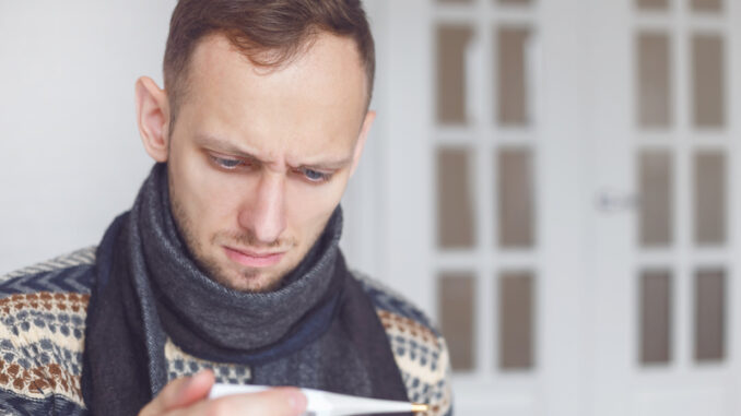 Sick man lying on sofa checking his temperature at home in the living room