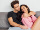 Selective focus of smiling woman touching boyfriend on sofa on grey