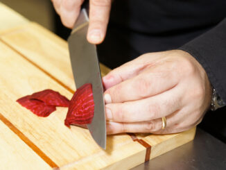 Professional chef cutting beet-root on wooden plank