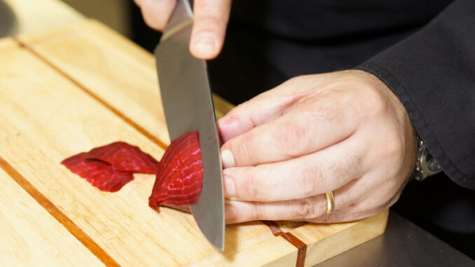 Professional chef cutting beet-root on wooden plank