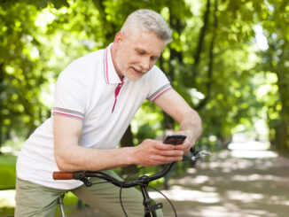 Mature smiling man using contemporary mobile phone at park