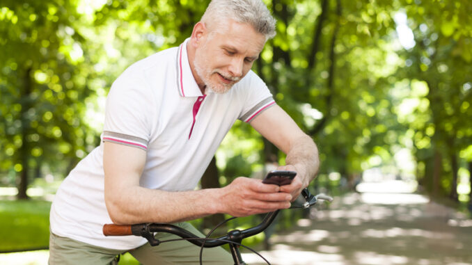 Mature smiling man using contemporary mobile phone at park