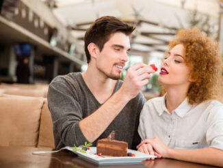 Portrait of a beautiful couple eating cake with strawberry in restaurant