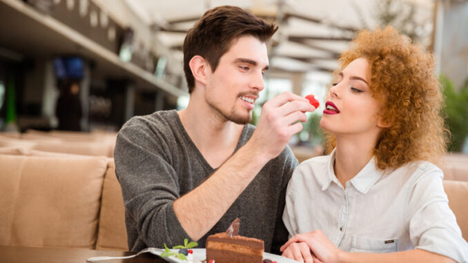 Portrait of a beautiful couple eating cake with strawberry in restaurant