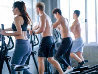 Beautiful sport women exercise with elliptical machine among the other men in the gym with day light