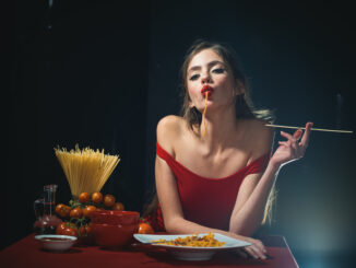 Young woman eating tasty pasta on black