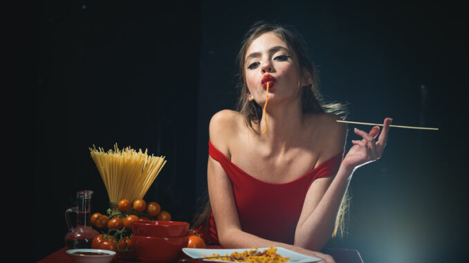 Young woman eating tasty pasta on black