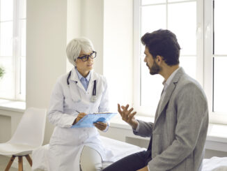 Worried man talking to doctor while sitting in exam room during consultation in modern clinic or hospital.