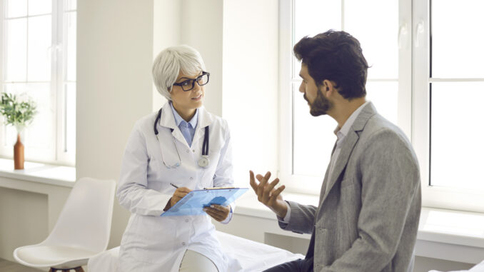 Worried man talking to doctor while sitting in exam room during consultation in modern clinic or hospital.