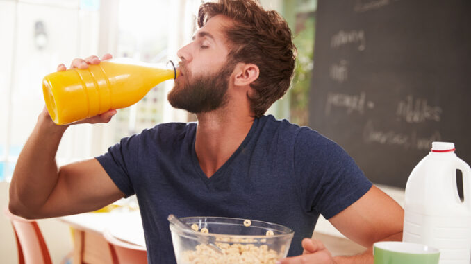 Young Man Eating Breakfast And Drinking Orange Juice