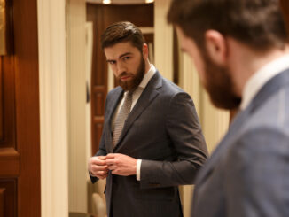 View from back of handsome bearded man looking at the mirror while being in a shop