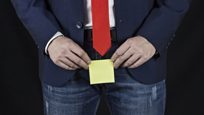 Man in suit, businessman holding sticker in his groin area