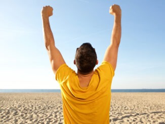 Portrait from back of man cheering with arms raised at the beach